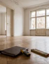 Leere Altbauwohnung mit Fischgrätparkett, davor Lasermessgerät, Zollstock und Mappe für die Ortsbesichtigung eines Gutachters
